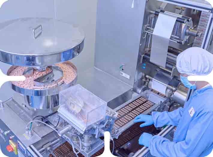 Worker in cleanroom operating an automated pill packaging machine, demonstrating operational excellence.